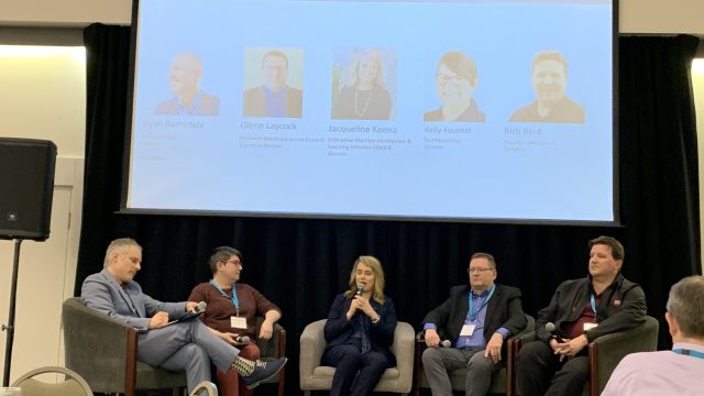 five people sitting in chairs on stage as part of panel discussion.